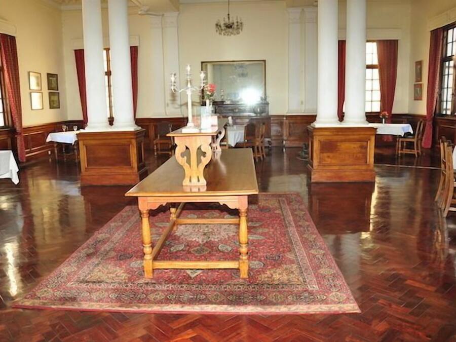 A spacious room with a large wooden table at the center, surrounded by chairs and a patterned rug.