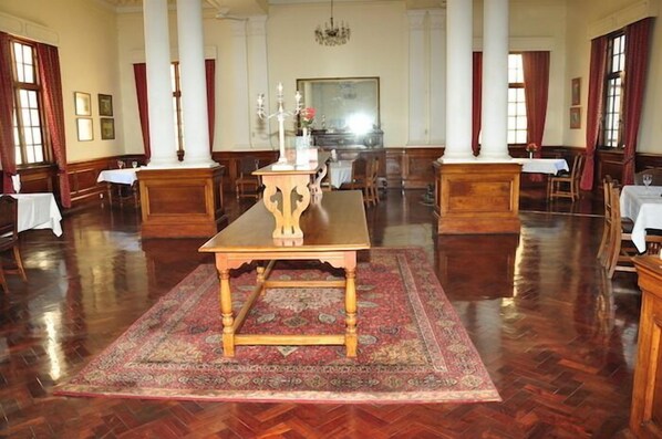 A spacious room with a large wooden table at the center, surrounded by chairs and a patterned rug.