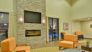 A modern living room with a stone wall, a flat-screen TV, a fireplace, and comfortable seating. - Comfort Suites near Westchase on Beltway 8 (Houston)