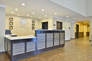 Una recepción con un fondo de pared de piedra, un letrero que dice "Comfort Suites" y un interior moderno y bien iluminado.