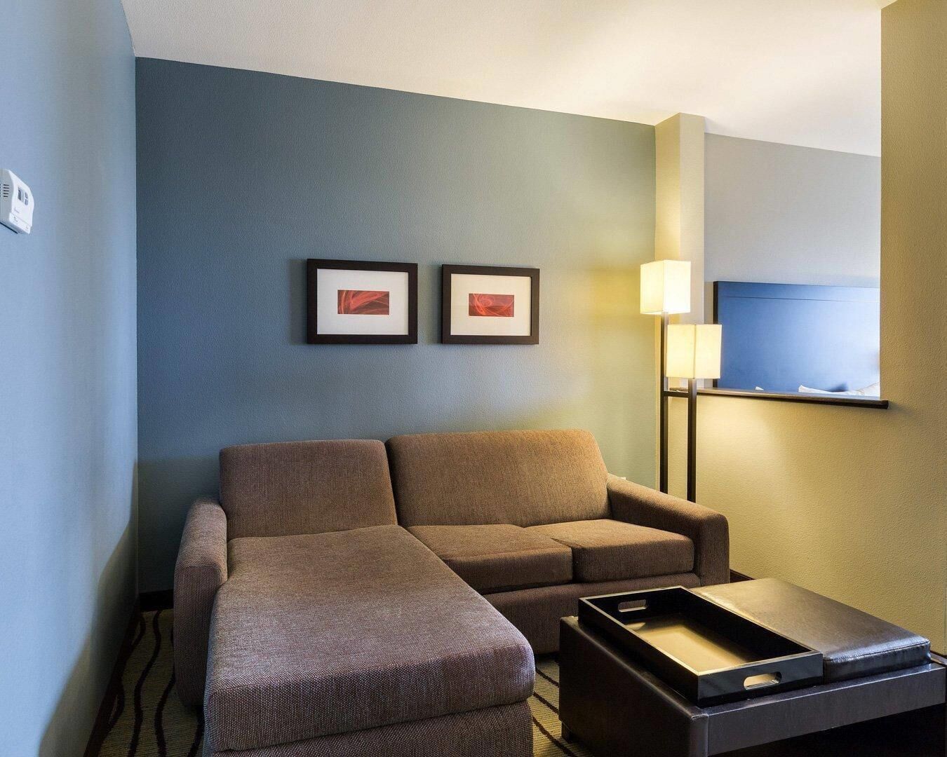 Habitación de hotel con sofá, una mesita, una lámpara y dos cuadros en la pared.