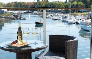 Un balcon avec une table dressée pour deux personnes, agrémentée d’une bouteille de vin et de verres, donnant sur une marina où sont amarrés des bateaux.