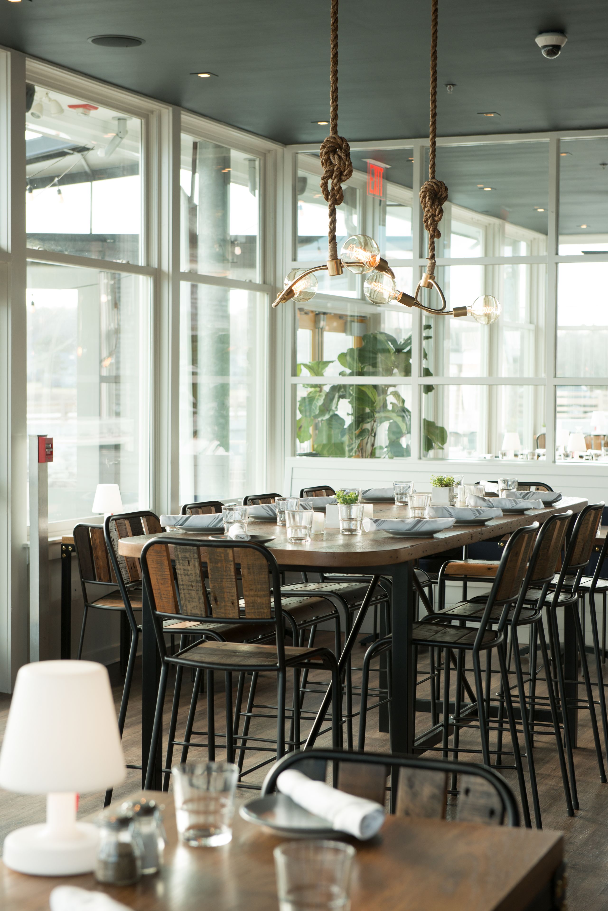 A dining area with a round table set for six, surrounded by black chairs, with a view of the city through large windows.