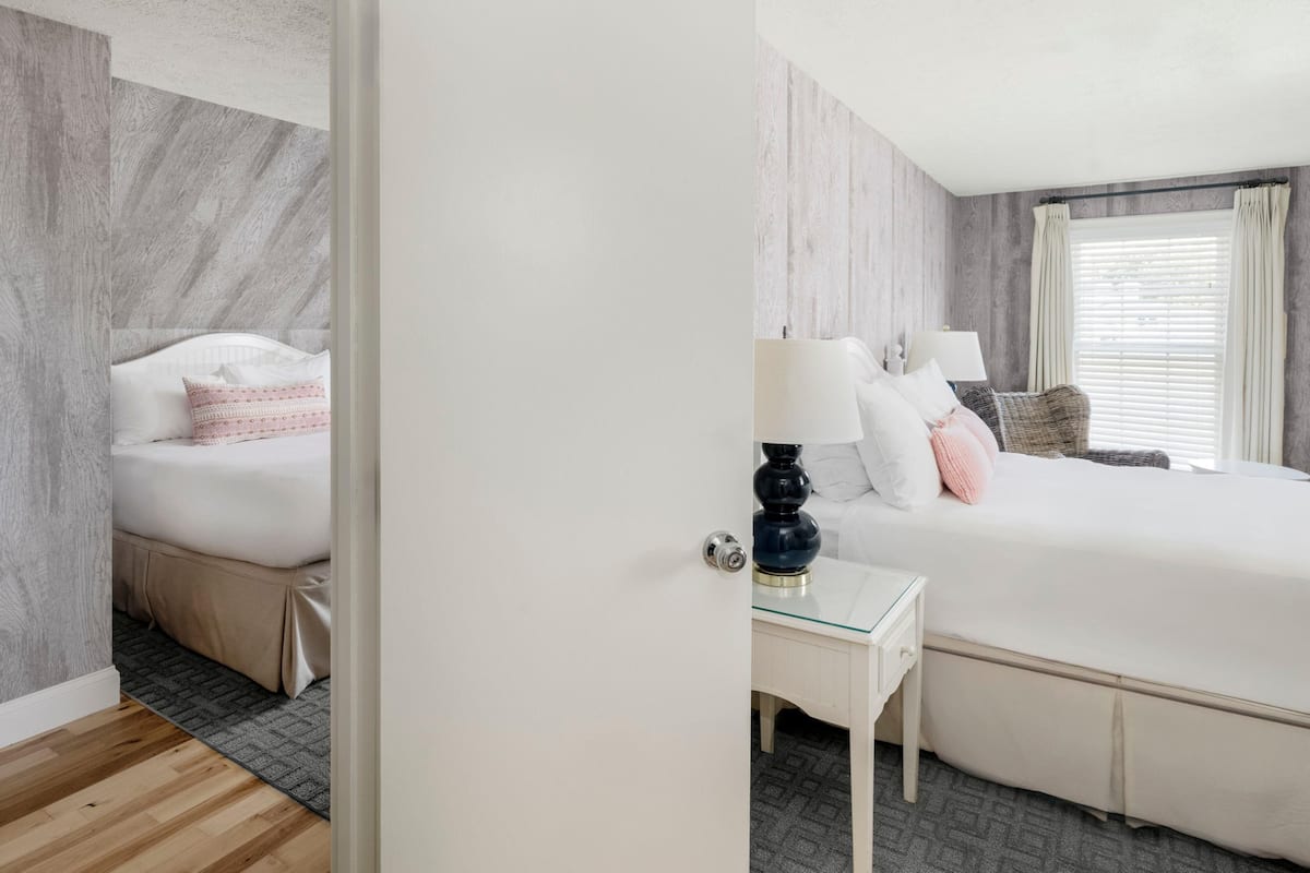 A hotel room with a bed, bedside table, lamp, and a window with curtains.