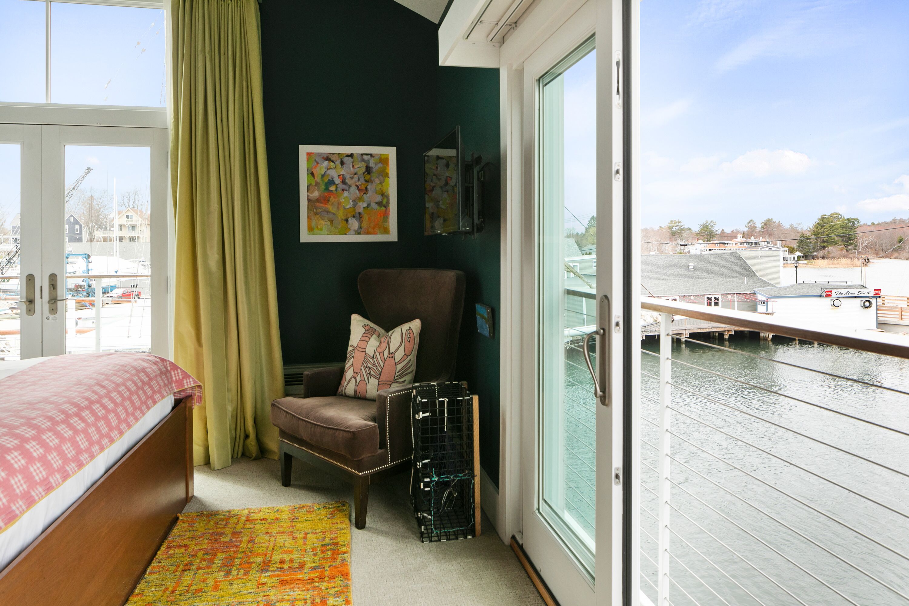 A room with a bed, a chair, a colorful rug, and a view of a water body.