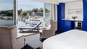 A hotel room with a large bed, two armchairs, a small table, a view of a marina with boats, and a blue accent wall. - The Boathouse Waterfront Hotel & Marina (Kennebunkport)