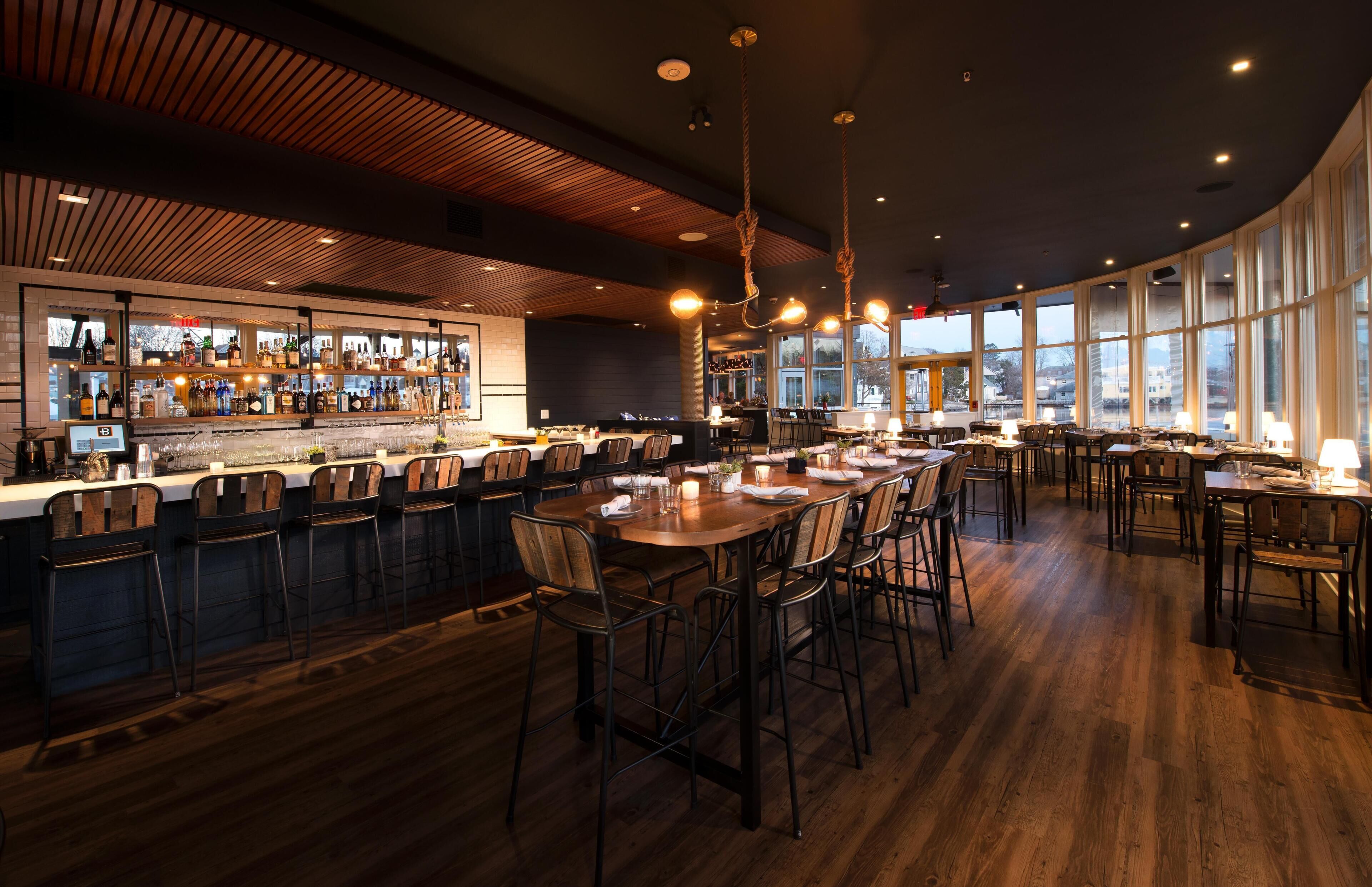 A restaurant with a bar area, wooden flooring, and large windows.