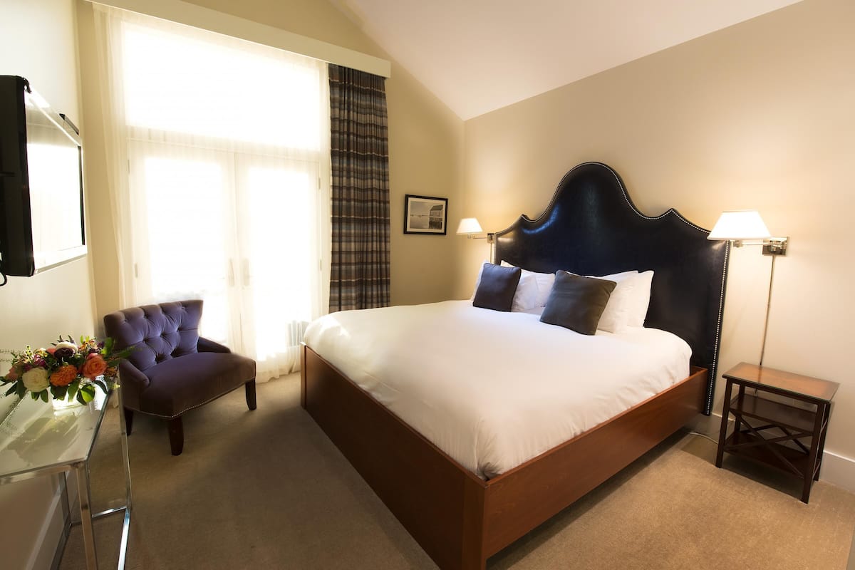 A neatly arranged hotel room with a large bed, a chair, a bedside table, and a lamp.