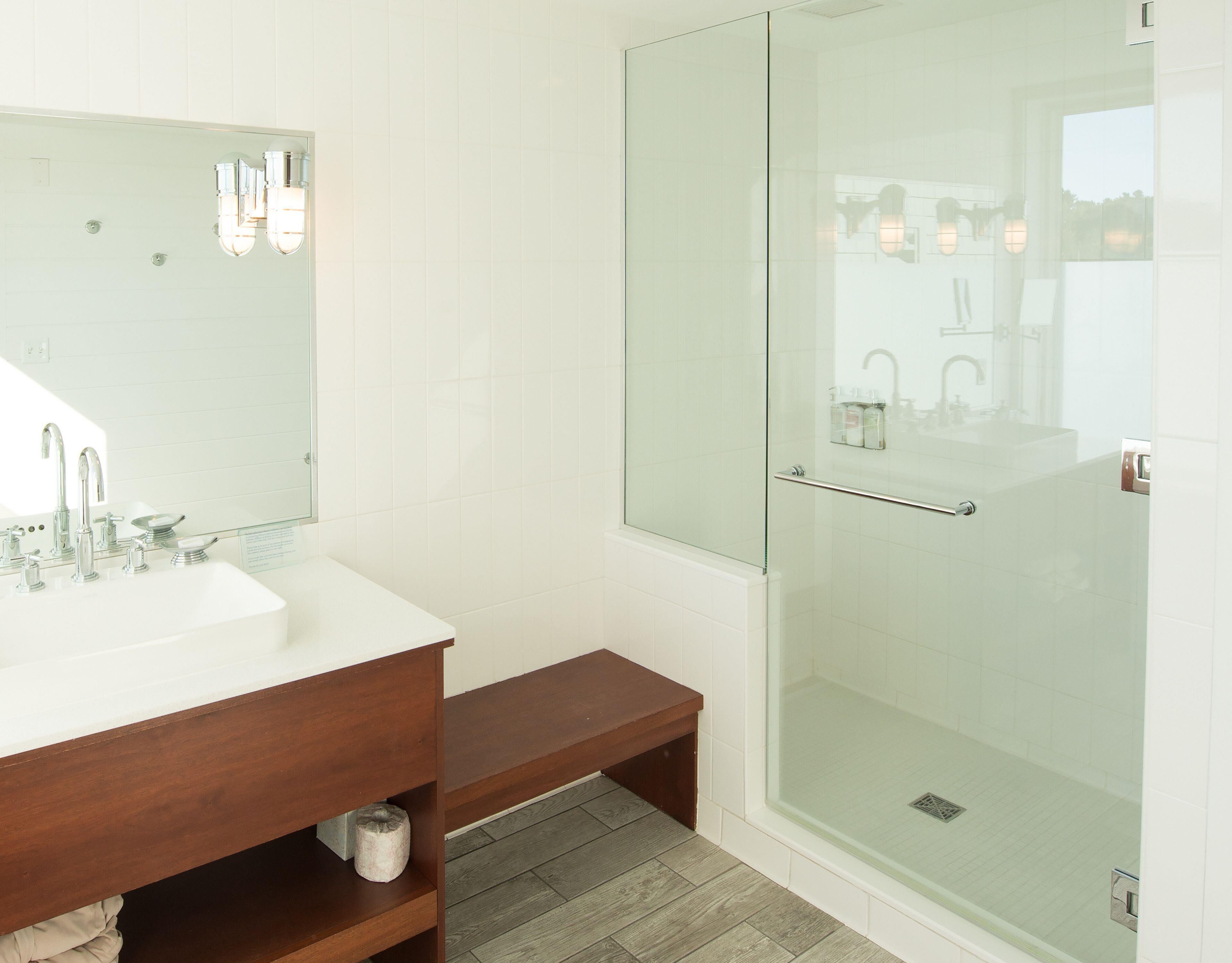 A modern bathroom with a glass shower enclosure, a white sink with a wooden vanity, and a large mirror.