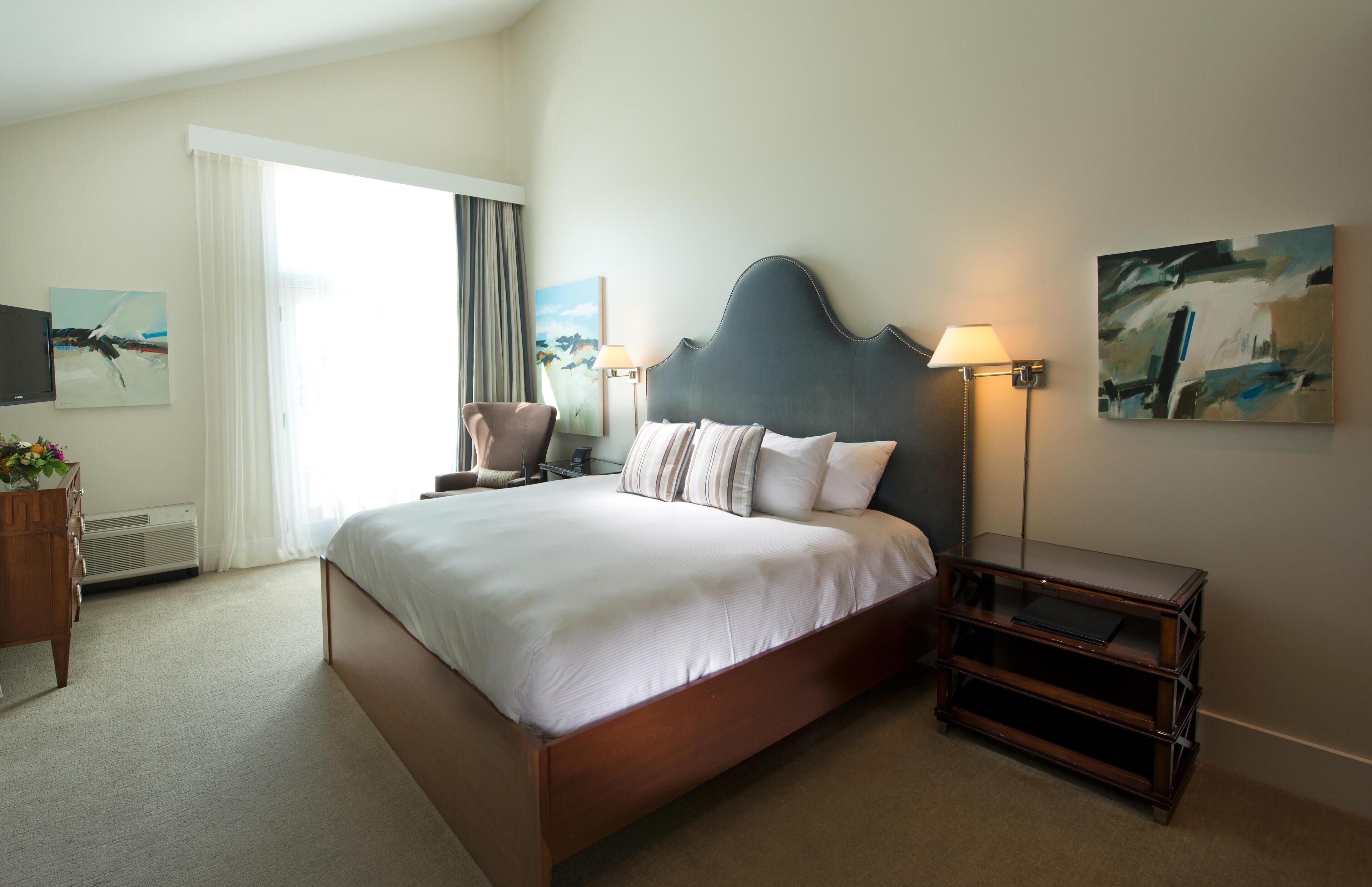 Ein Hotelzimmer mit einem großen Bett, einem Nachttisch, einem Sessel, einem Fernseher und einem Bild an der Wand.