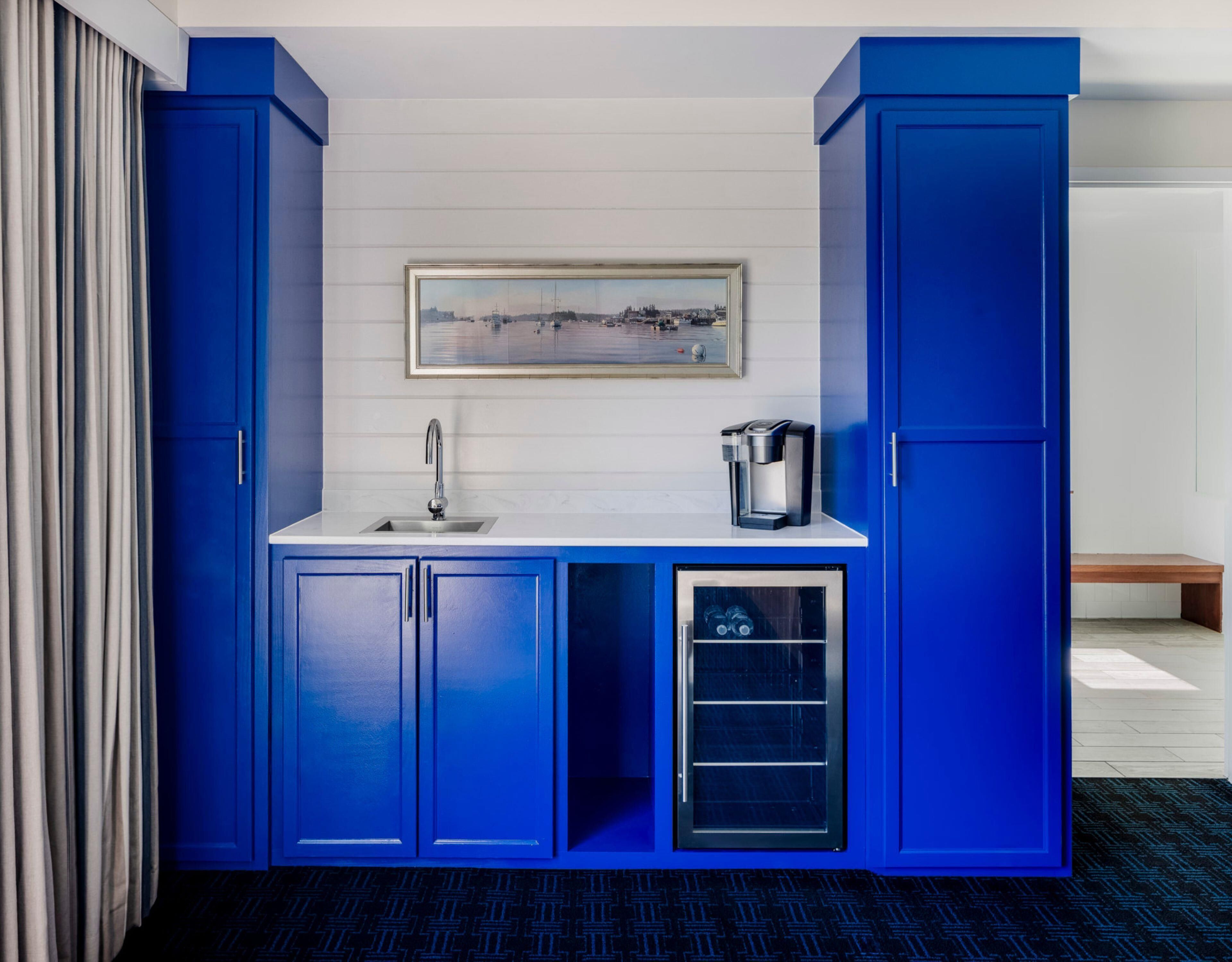 A compact kitchenette with blue cabinets, a coffee maker, and a sink.
