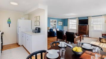 Une cuisine moderne avec des meubles blancs, un coin repas comprenant une table en bois, des chaises et un mur bleu.