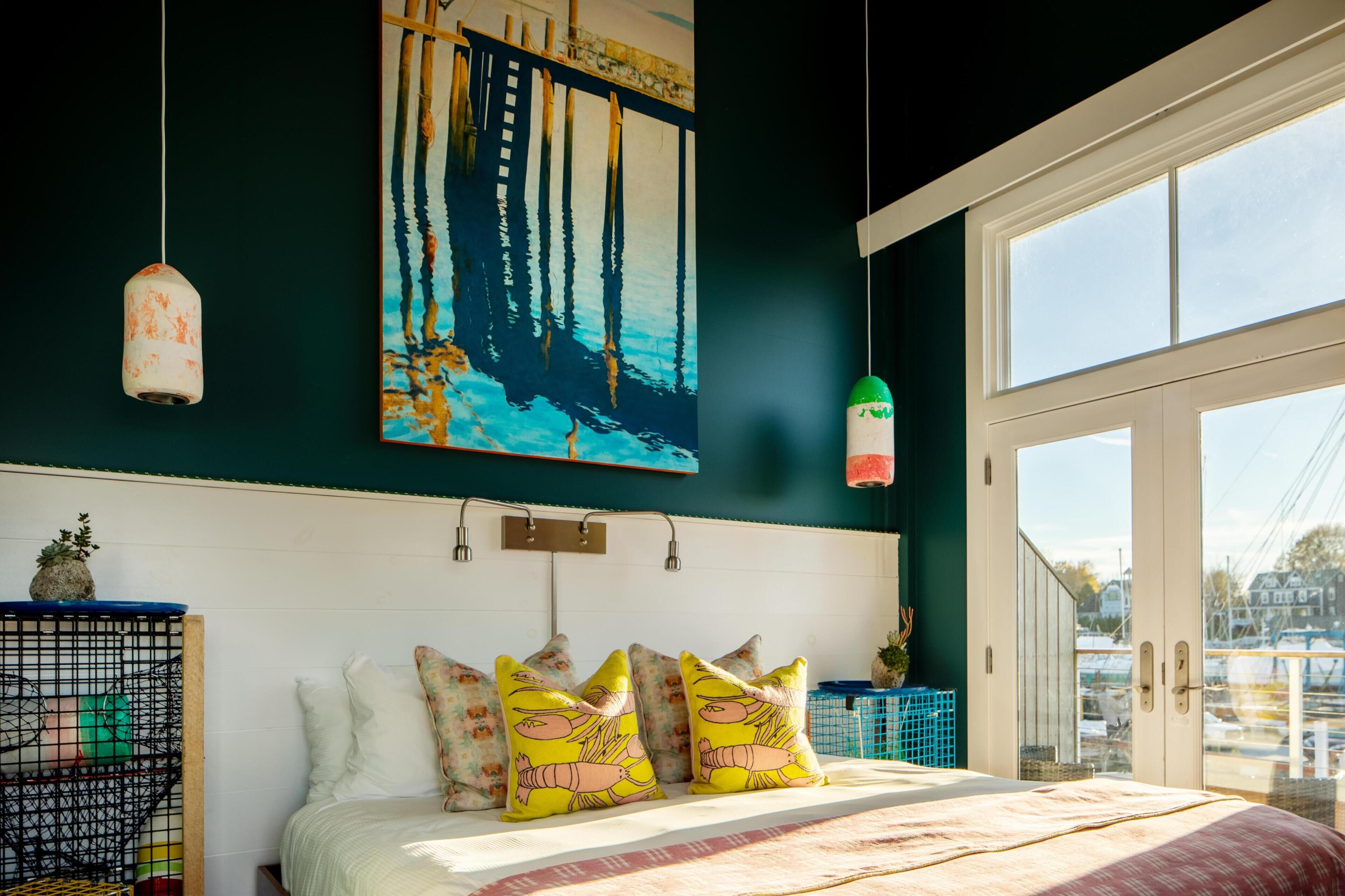 A bedroom with a bed, pillows, a painting, and a view through a window.