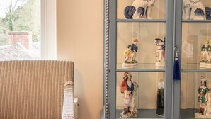 Una habitación con un sofá de mimbre, un aparador azul con puertas de cristal que exhibe figuras, y un cuadro en la pared.