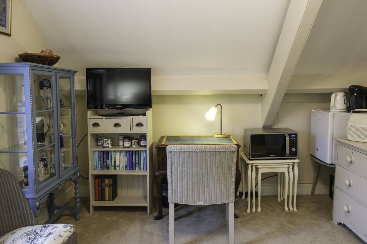 A compact living space with a television, bookshelves, a microwave, and a small dining table.