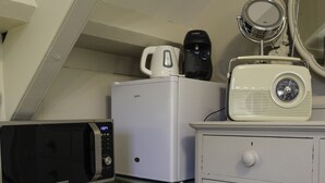 Una kitchenette compacta con microondas, un refrigerador blanco, cafetera, radio y espejo sobre un tocador.