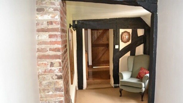 A room with exposed brick walls, a wooden door, a light-colored armchair, and a carpeted floor. - Woodview Bed & Breakfast (Colchester)