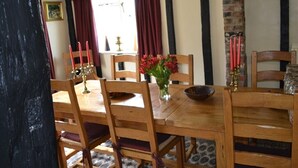 A dining area with a wooden table and chairs, a vase with flowers, and a brick wall. - Woodview Bed & Breakfast (Colchester)