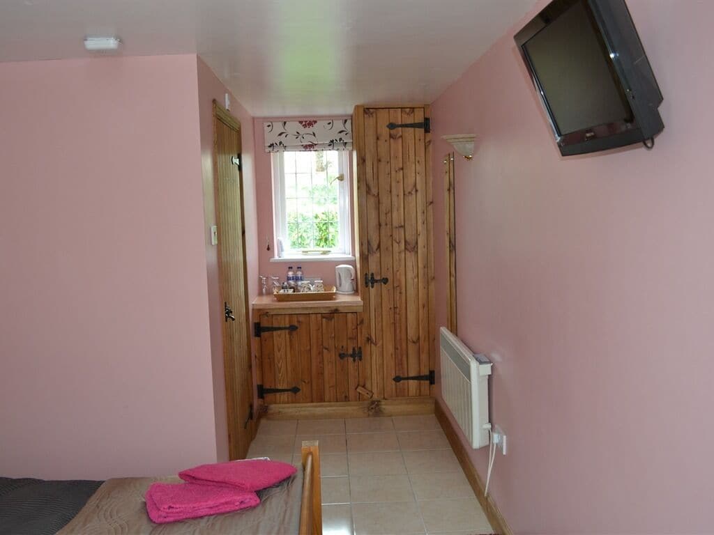 A small room with a bed, a wooden cabinet, a window with curtains, a radiator, and a television mounted on the wall.