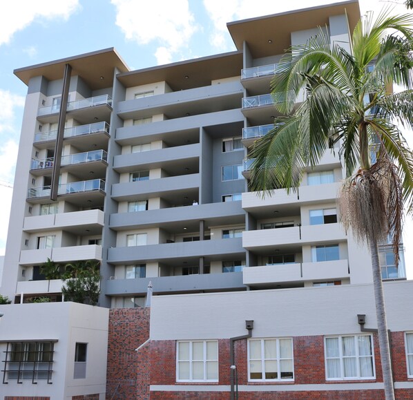 A multi-story residential building with balconies, brick lower floors, and a palm tree in the foreground. - Frisco Apartments (Spring Hill)
