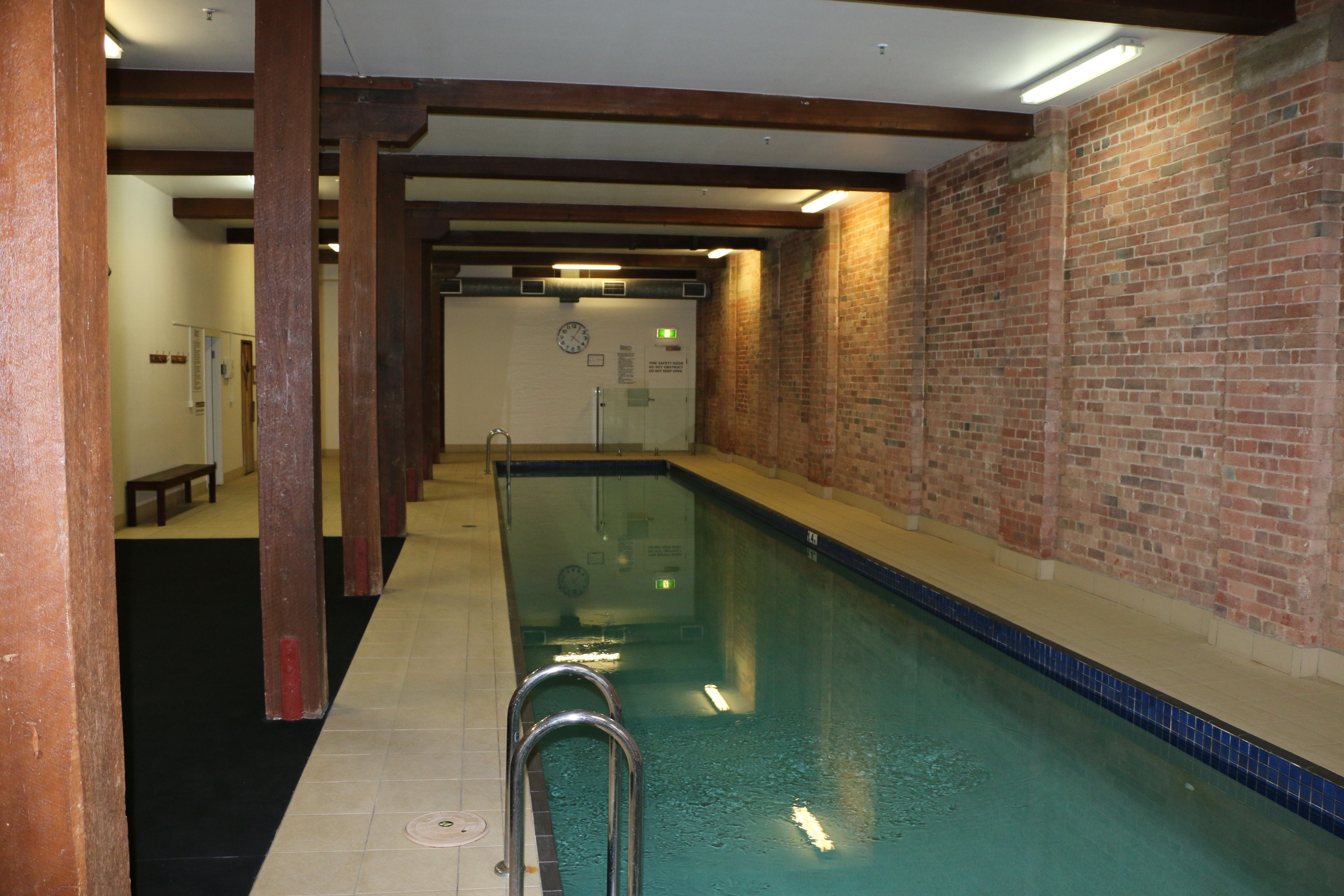 A swimming pool with a tiled floor, metal handrails, and a brick wall.