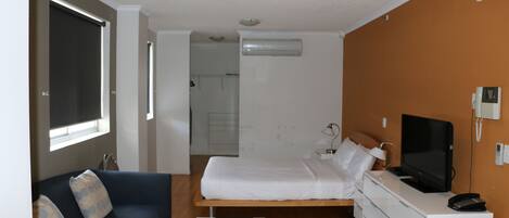 Ein modernes Hotelzimmer mit Bett, Sofa, Fernseher und Schreibtisch.
