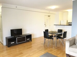 Ein modernes Wohnzimmer mit Holzboden, einem Esstisch mit Stühlen, einer schwarzen Unterhaltungseinheit und einem Sofa.