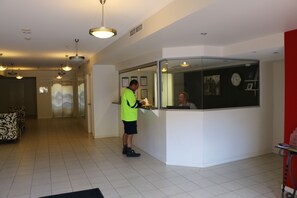 A reception area with a receptionist, a glass partition, and a clock on the wall. - Frisco Apartments (Spring Hill)