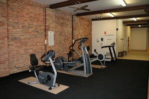 A gym with exercise equipment, a brick wall, and a ceiling fan. - Frisco Apartments (Spring Hill)