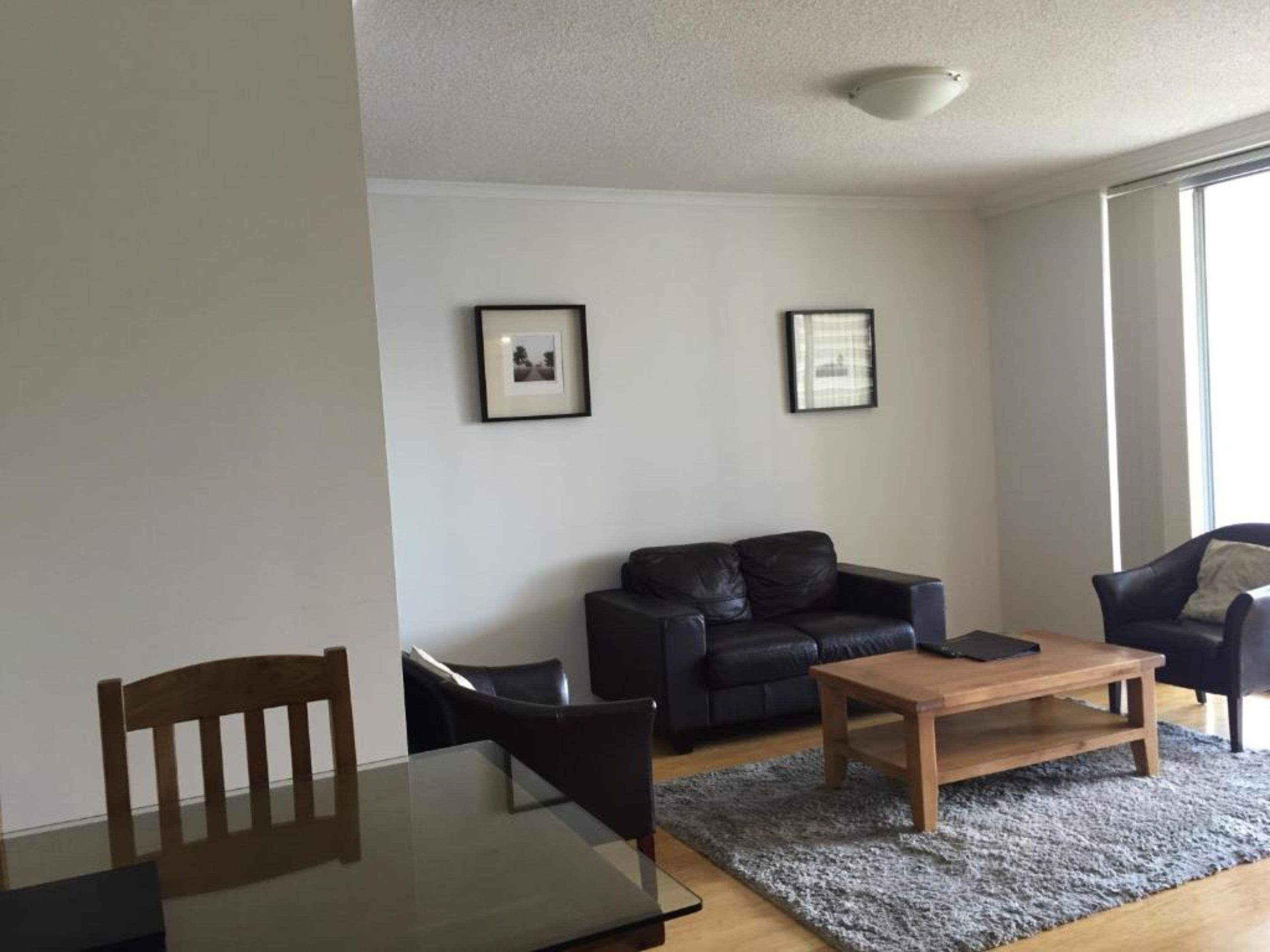 Un salon moderne avec une table basse en bois, un canapé en cuir noir et une table à manger avec des chaises. Deux tableaux encadrés ornent le mur.