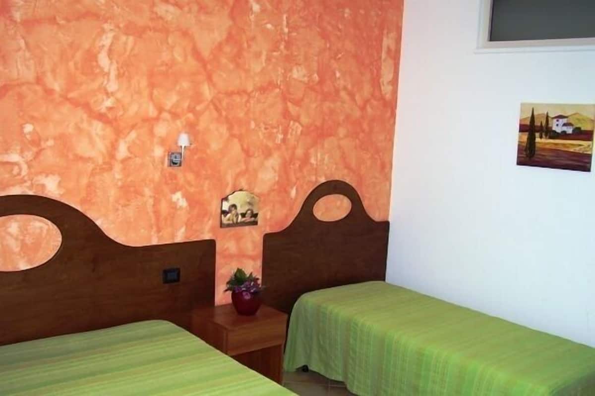 Una habitación con dos camas, cabecera de madera, una mesita con una planta y un cuadro colgado en la pared.
