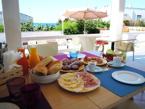 A breakfast table with croissants, pastries, eggs, and ham, with a view of the sea and greenery in the background. - Vistamare Bed and Breakfast (Alliste)