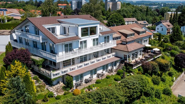 Una casa de dos pisos con un balcón, un patio con muebles de exterior y un jardín.