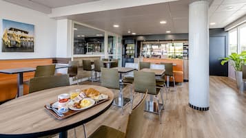 Un espace de restauration moderne, doté de plusieurs tables et chaises, d’un pilier central et offrant une vue sur la cuisine.