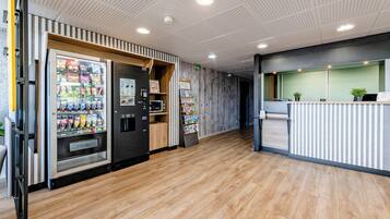 A modern interior with a wooden floor, a vending machine, a microwave, and a reception desk.