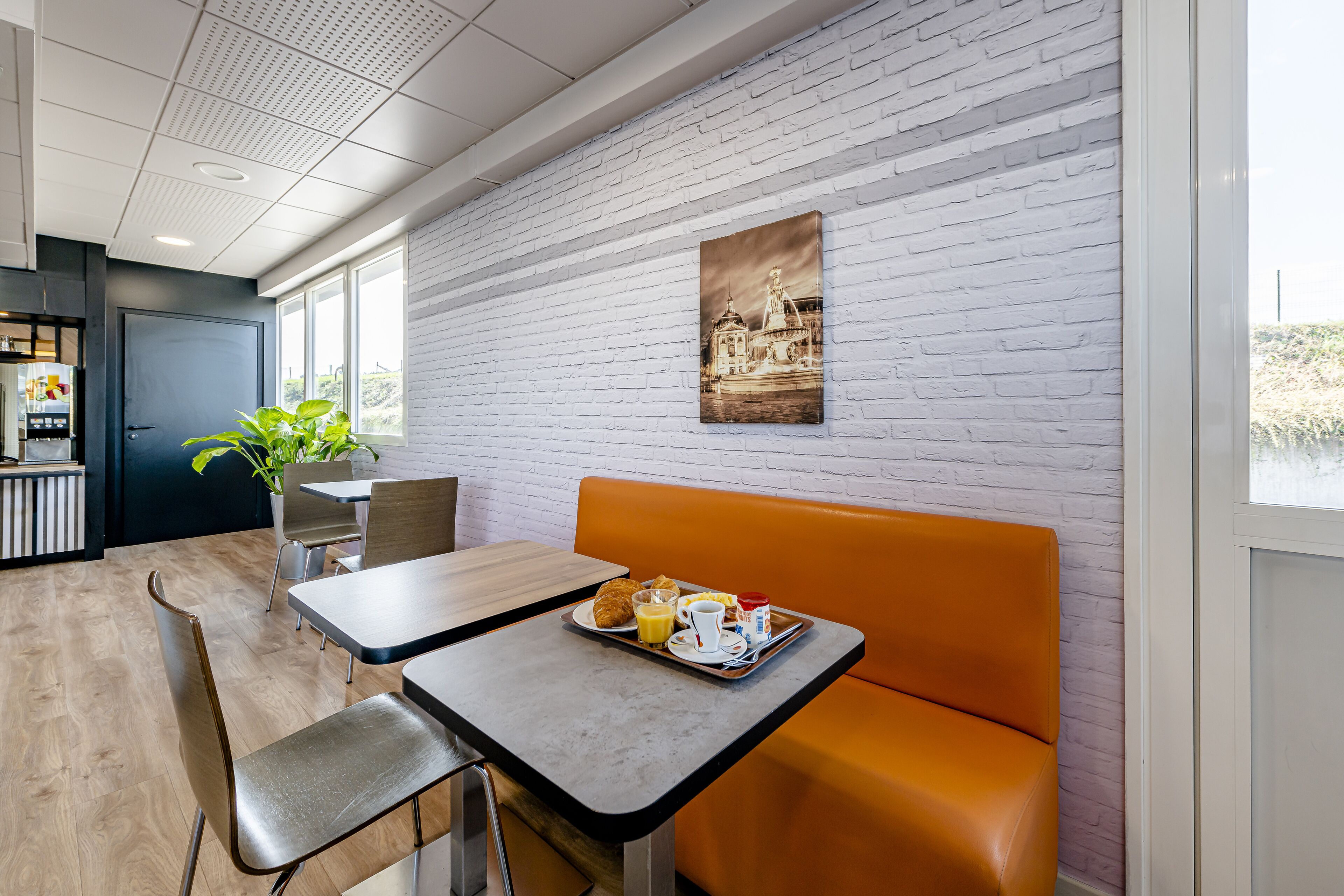 A modern dining area with a white brick wall, a painting, and a table with a tray of food and drinks.