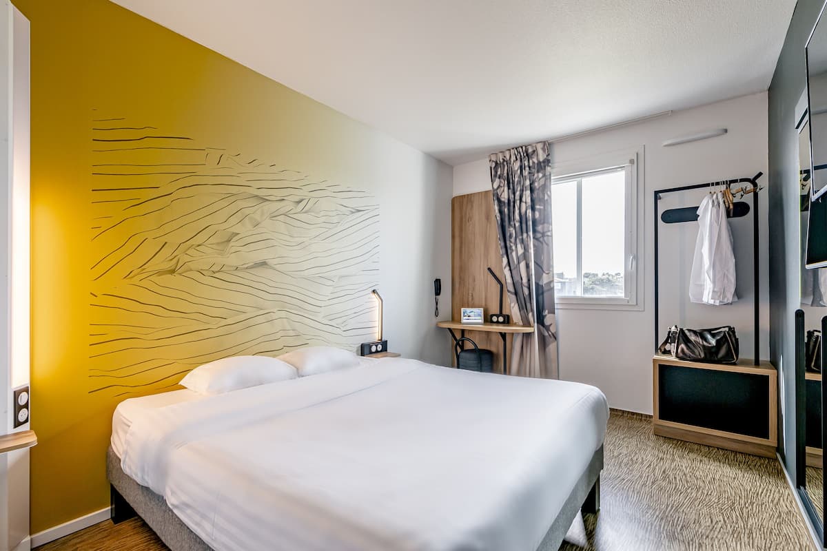 Une chambre d’hôtel moderne équipée d’un grand lit, d’un bureau avec un ordinateur, d’un miroir et d’une armoire.