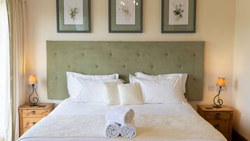 Un lit bien fait, avec du linge de lit blanc, deux tables de chevet avec des lampes, et trois œuvres d’art florales encadrées accrochées au mur.