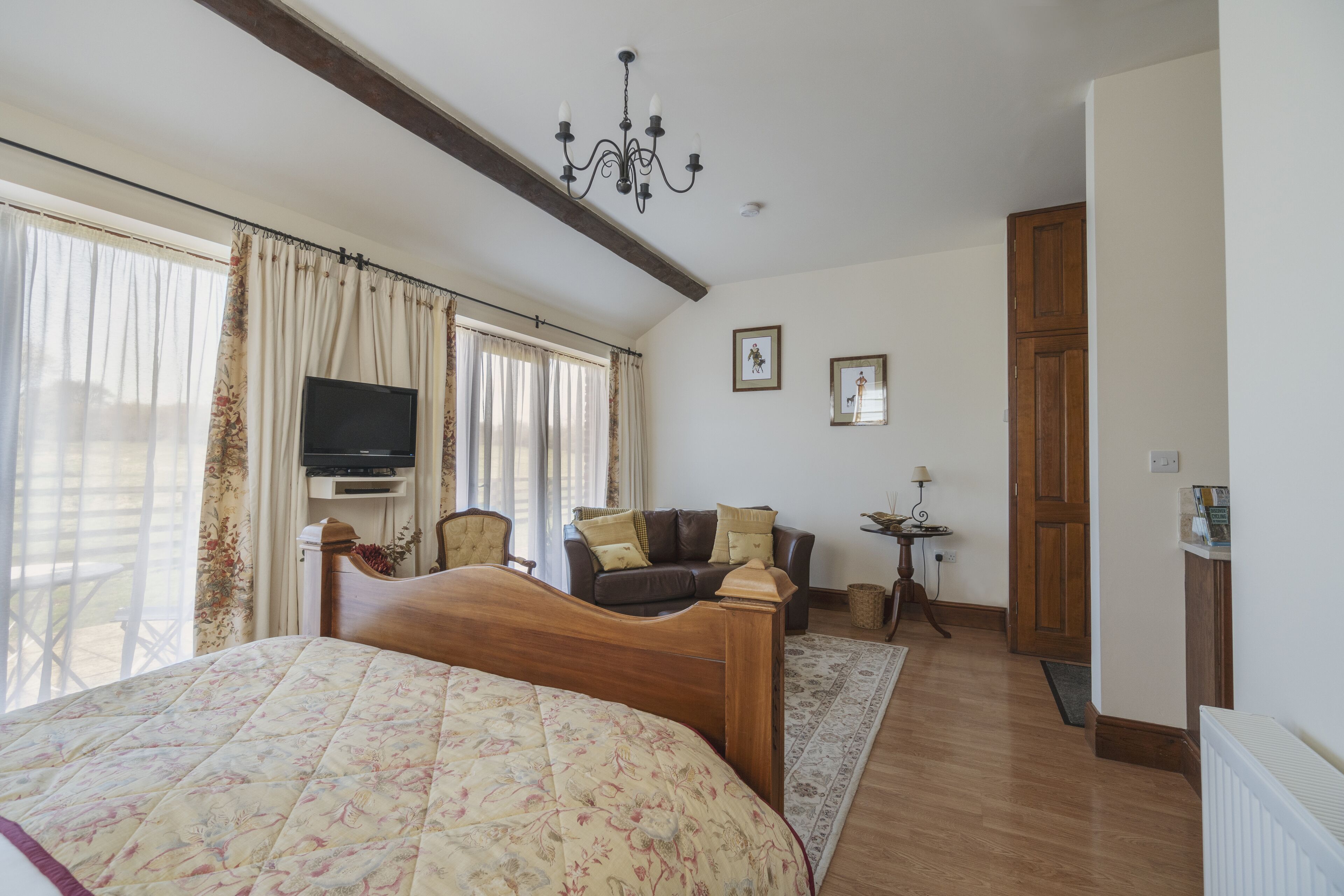 A bedroom with a bed, a sofa, a TV, and a chandelier.