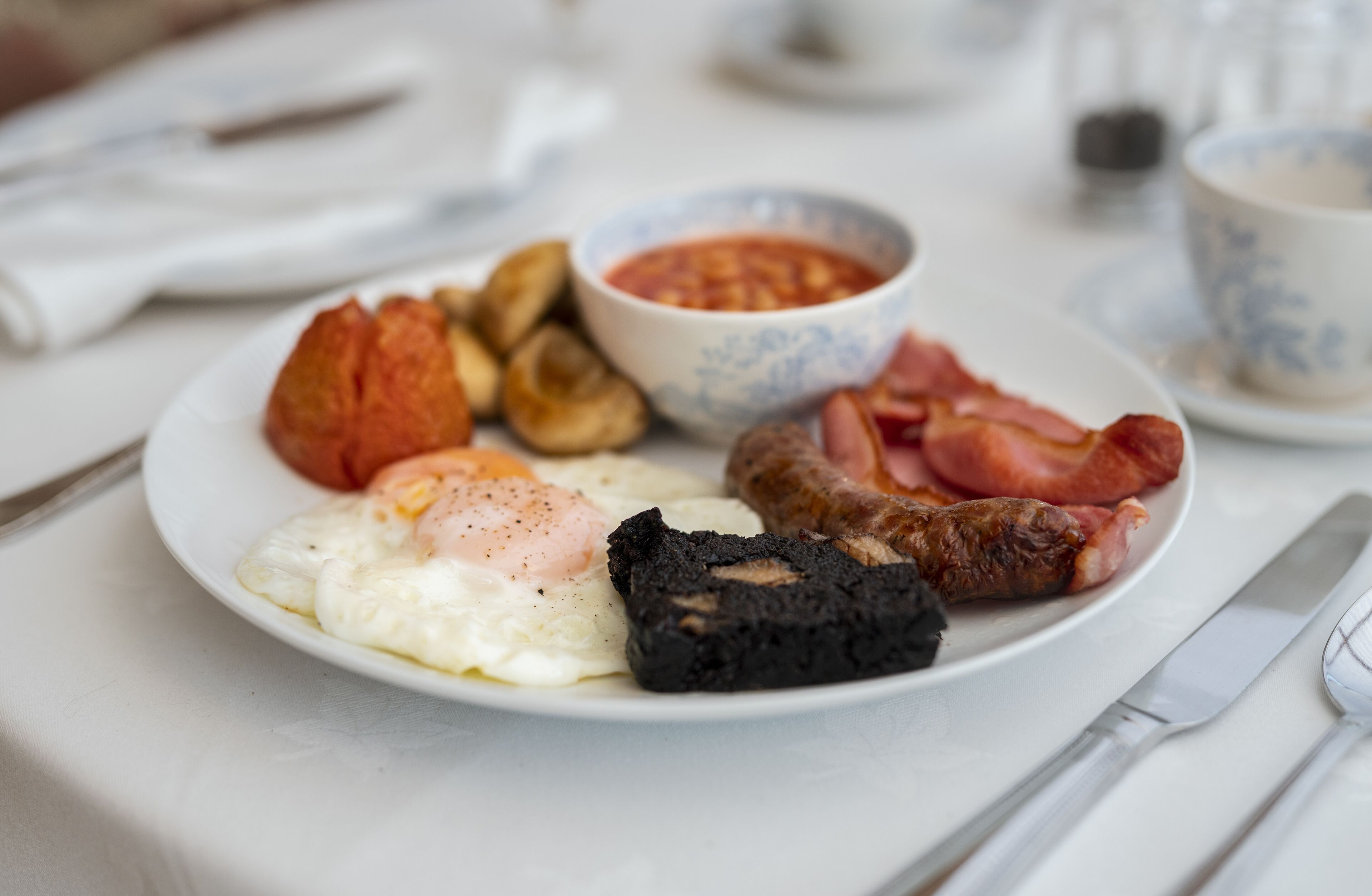 Un plato de desayuno con huevos, salchichas, tocino, champiñones y un tazón de salsa.