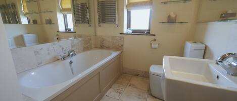 A bathroom with a bathtub, a sink, and a toilet. There are shelves with toiletries and a window with a towel rack.