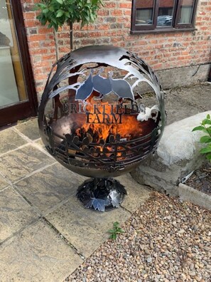 A metal sculpture with a fire pit, labeled "BRICKFIELD FARM," set on a stone patio.