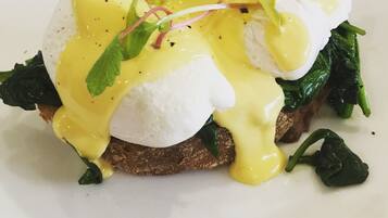 A breakfast dish with poached eggs, hollandaise sauce, spinach, and microgreens.