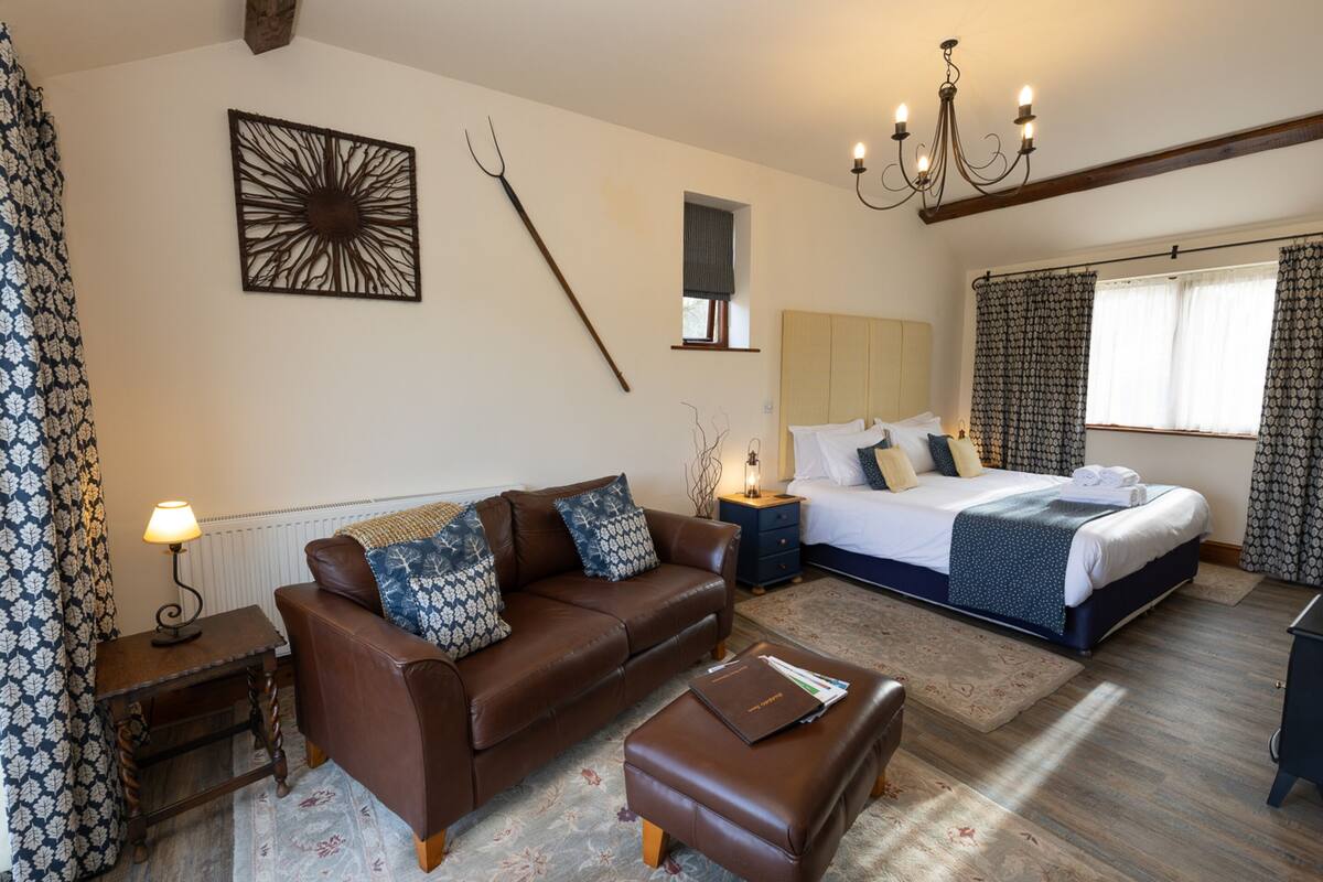 Quarto com cama, sofá de couro marrom, mesa de cabeceira, escrivaninha e lustre.
