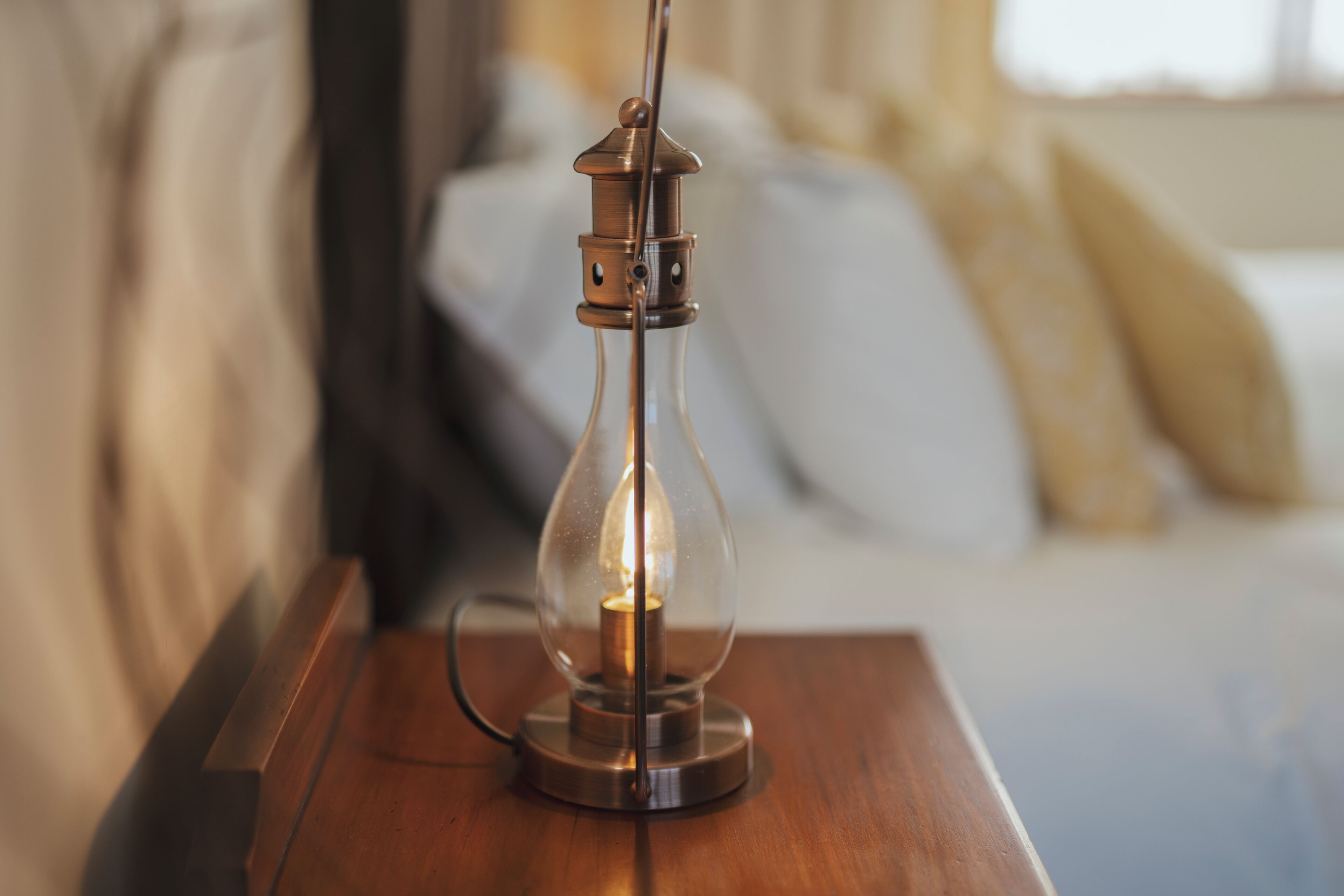 A clear glass table lamp with a visible light bulb on a wooden table.