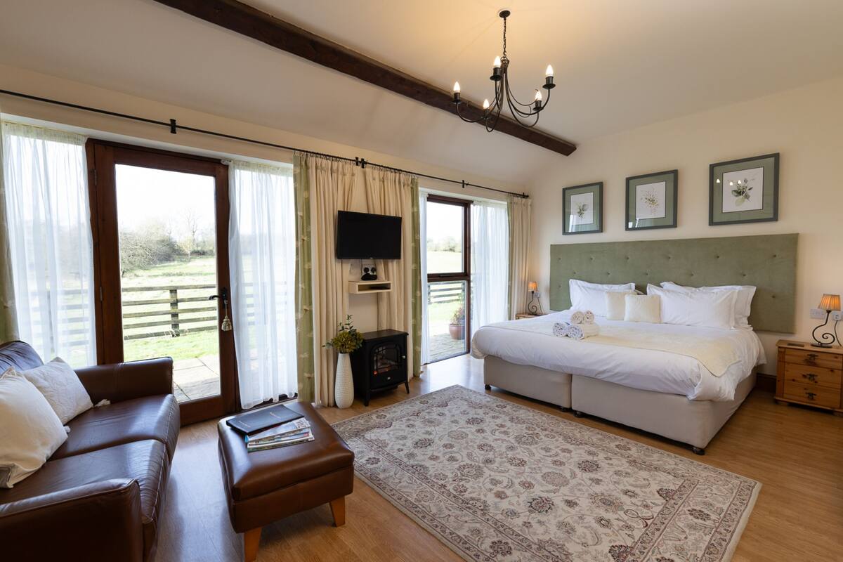 Quarto com cama grande, sofá, televisão e vista para o exterior.
