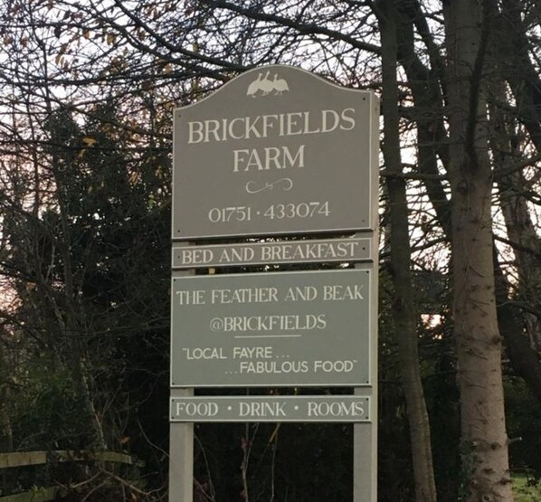 A sign for Brickfields Farm advertising bed and breakfast, local fare, and food, drink, and rooms.