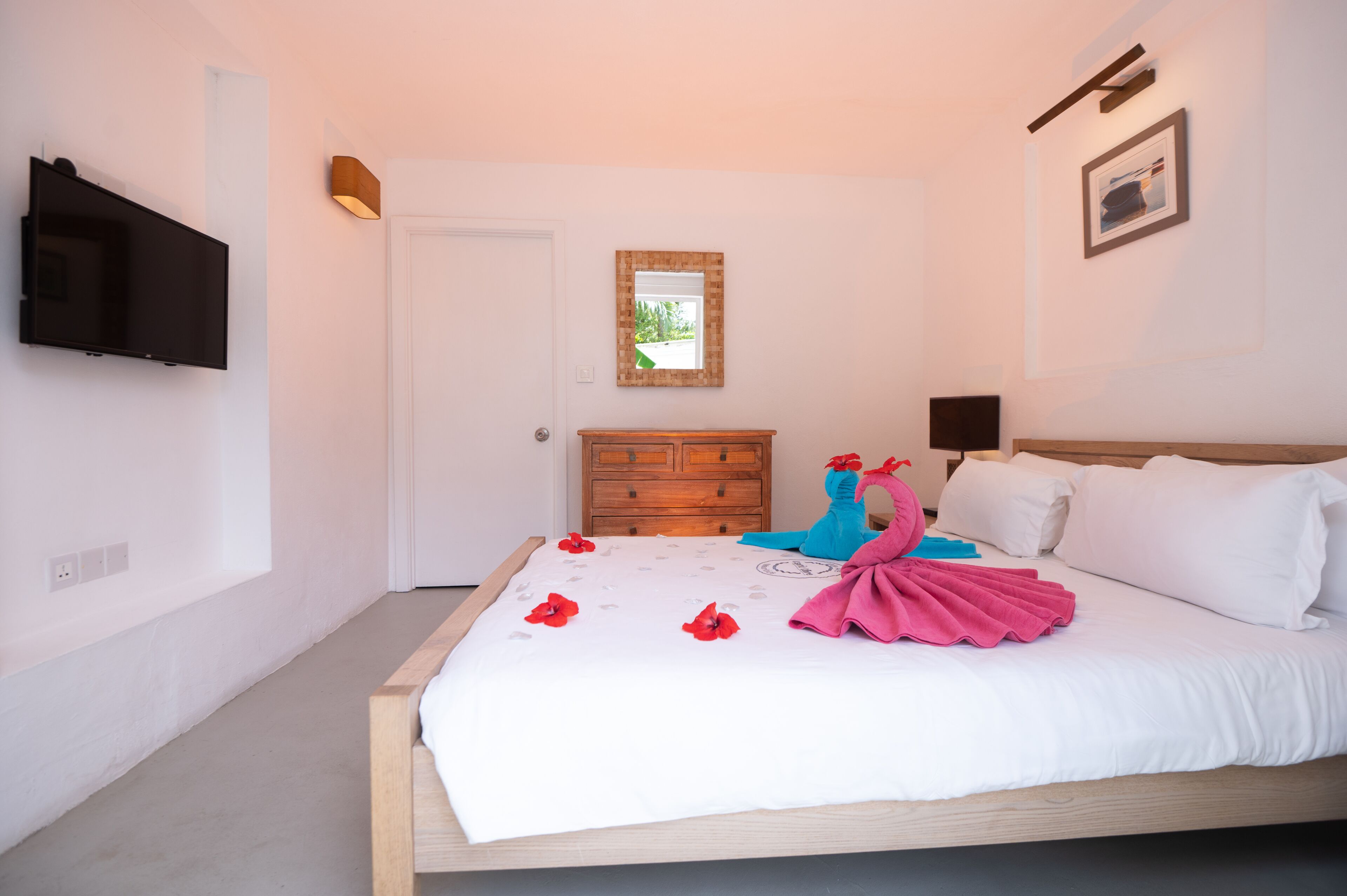 Una camera da letto con un letto, una TV a parete, una cassettiera in legno e uno specchio.