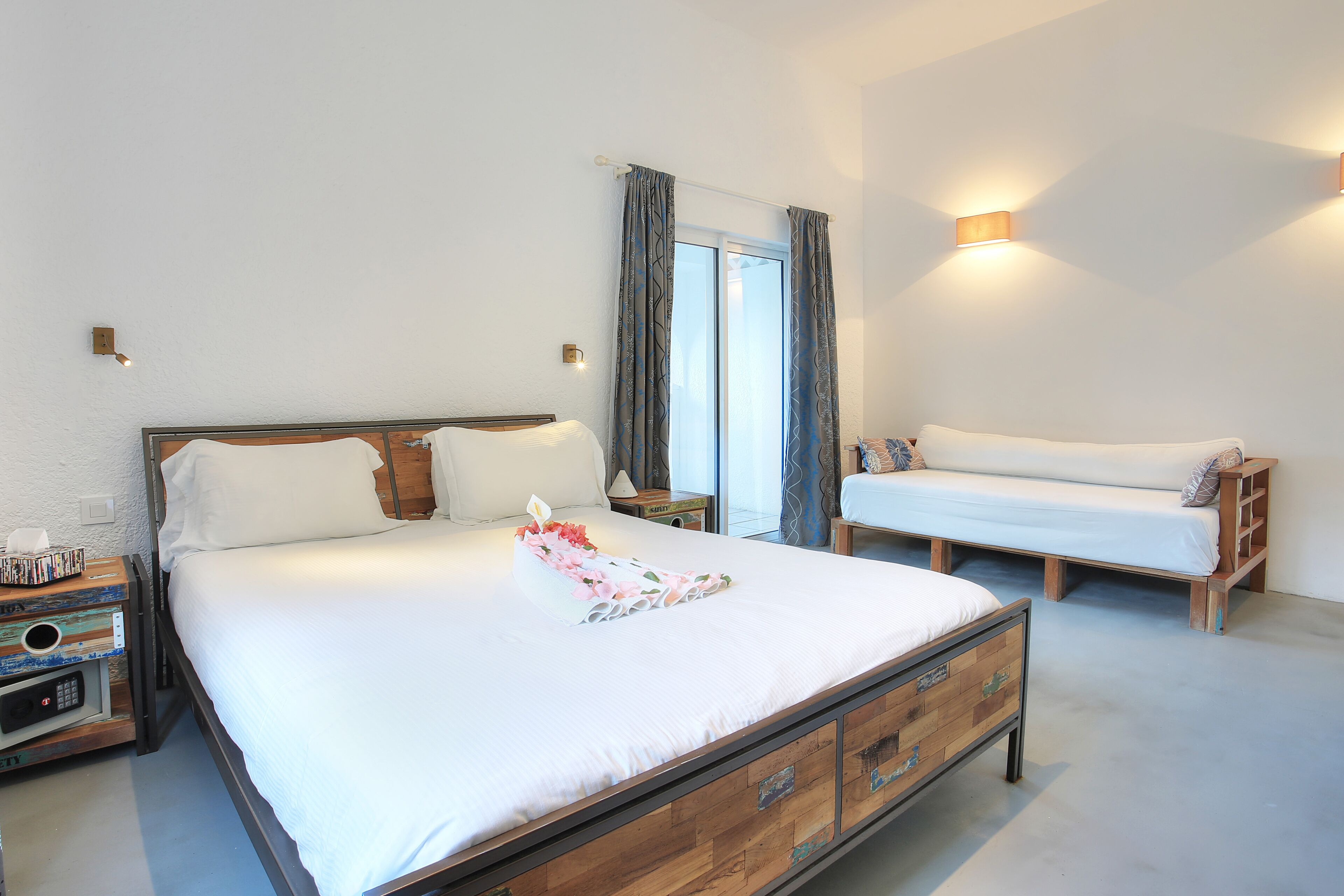 Une chambre à coucher avec un grand lit, des tables de chevet, un banc et une fenêtre avec des rideaux.
