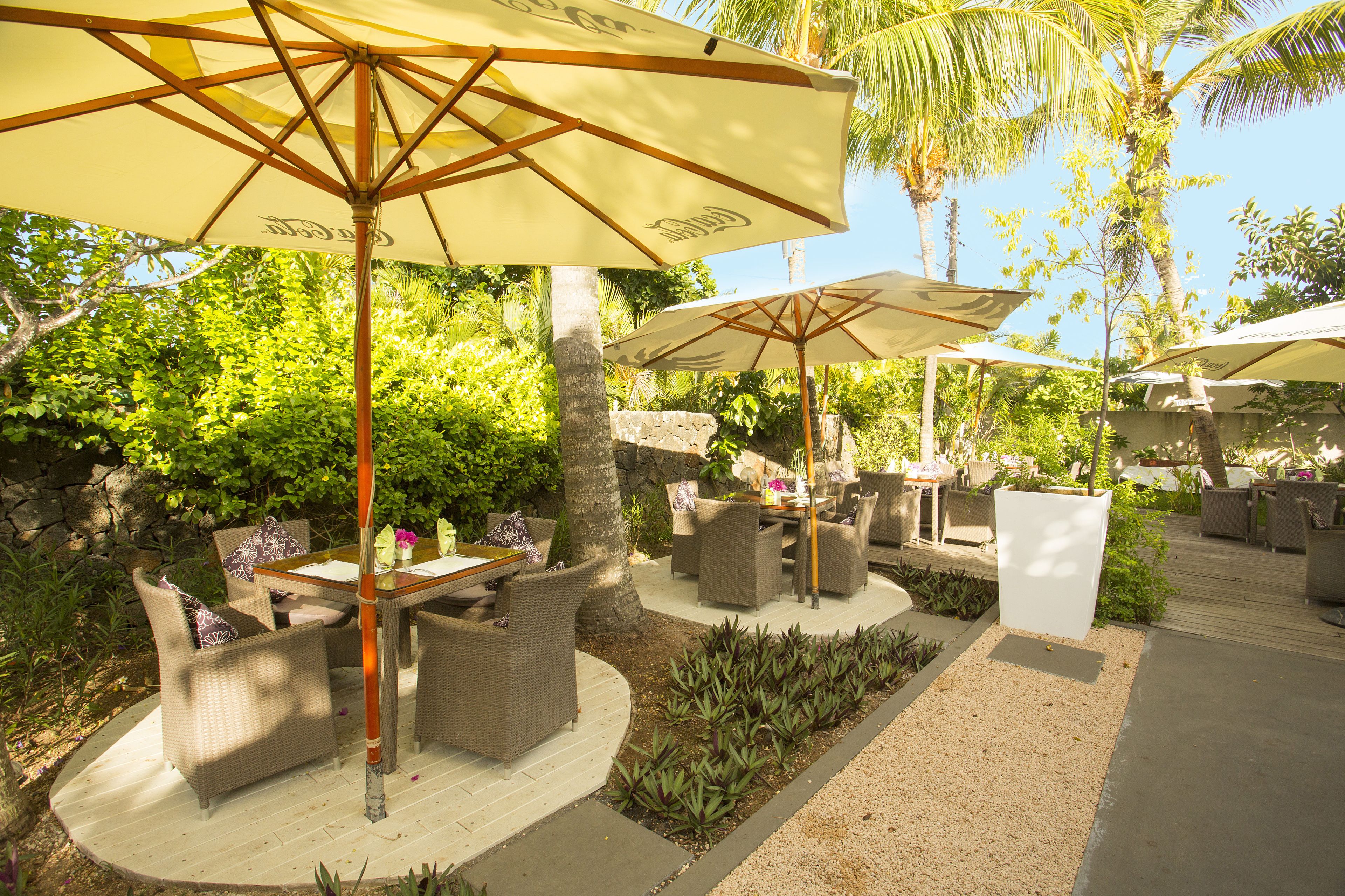 An outdoor patio area with wicker furniture, umbrellas, and a stone wall.